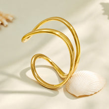 Gold double loop cuff bracelet displayed in a curved flat lay on a neutral surface