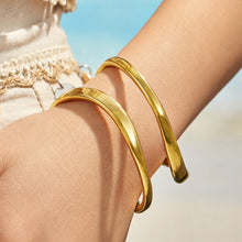Gold double loop cuff bracelet styled with layered bracelets on a model wrist