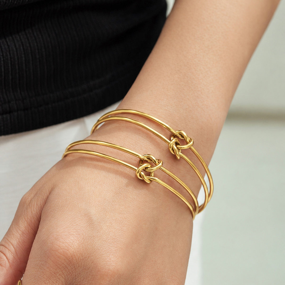 Gold-tone double wire open cuff bracelet with sculptural knot detail worn on wrist