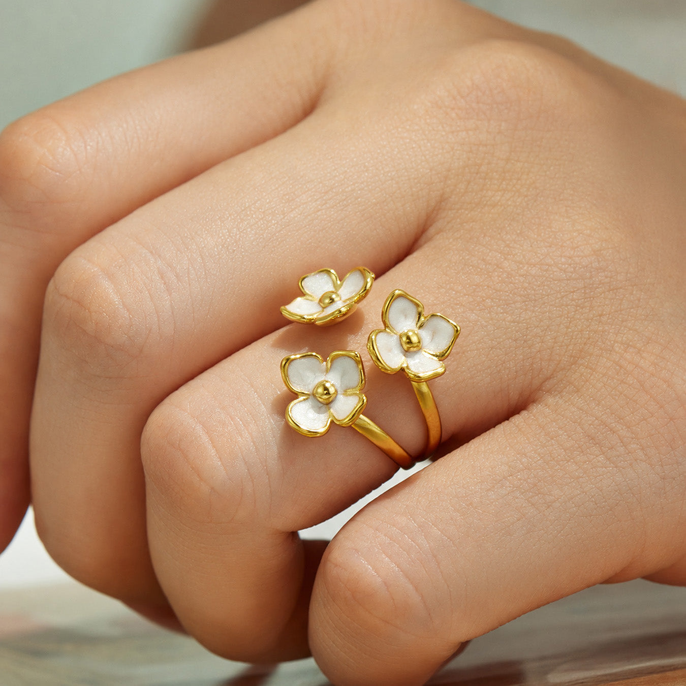 Close-up of a gold enamel small flower open ring worn on a model finger