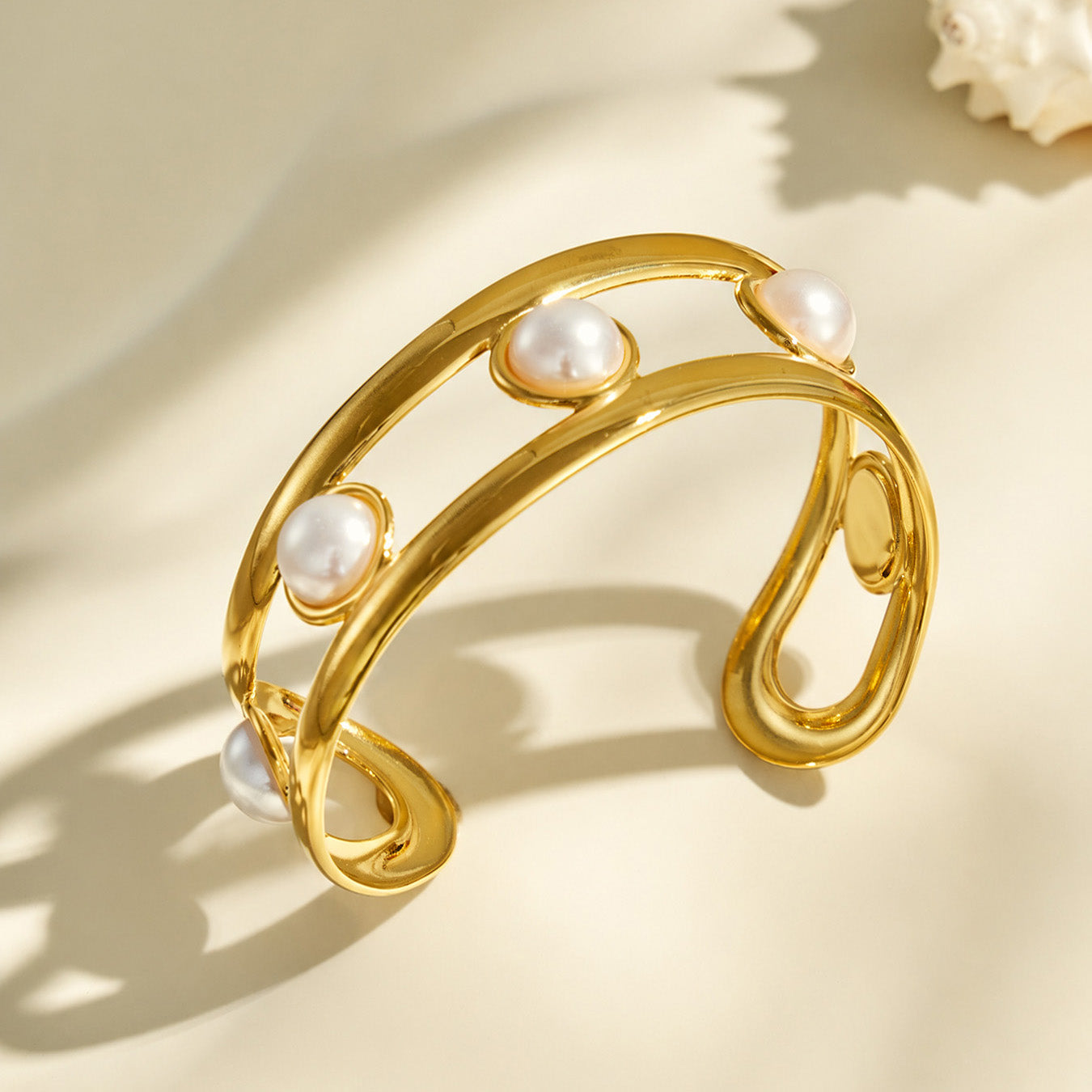Angled product view of a gold cuff bracelet with white faux pearl accents