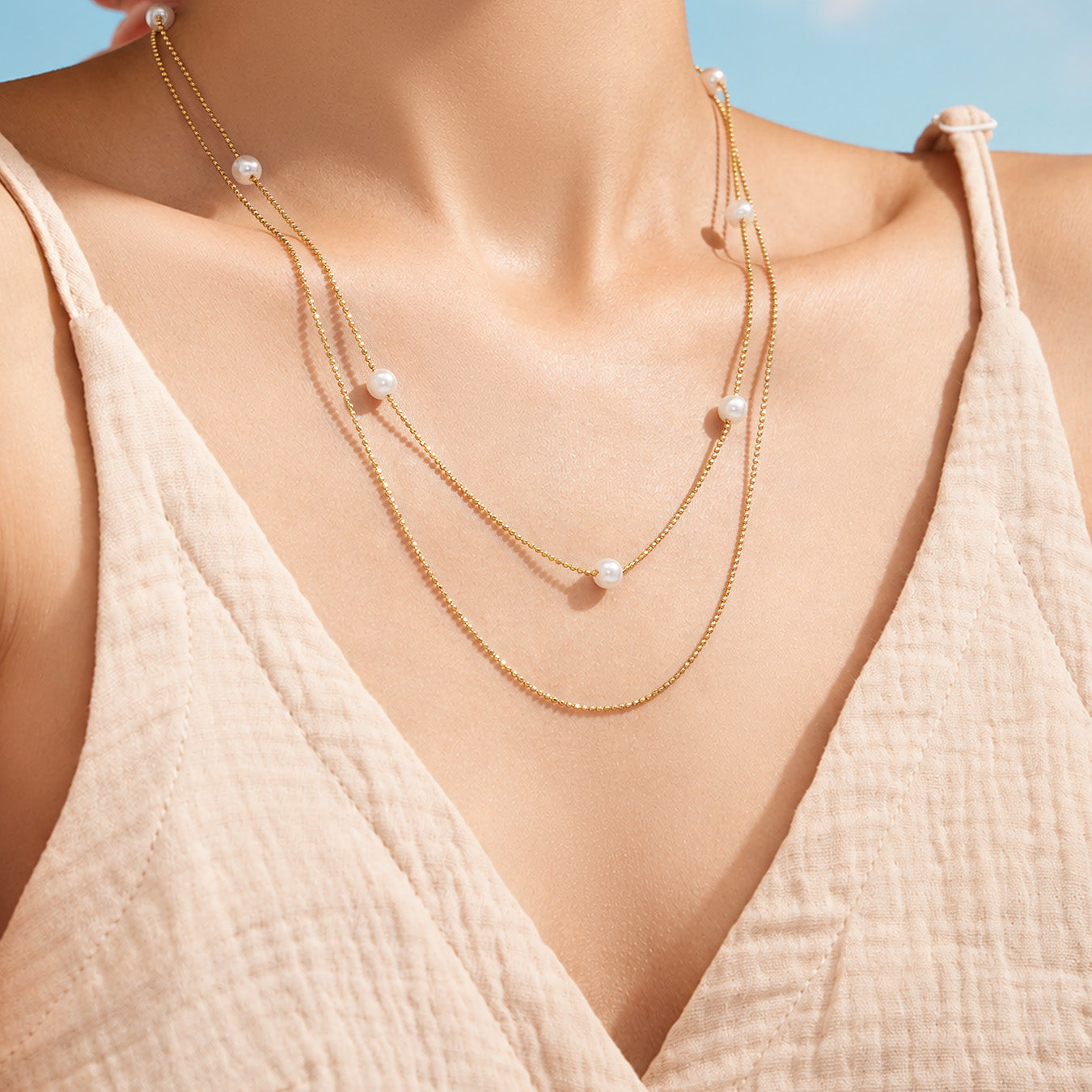 Model styling a gold faux pearl layered necklace with a neutral V-neck outfit