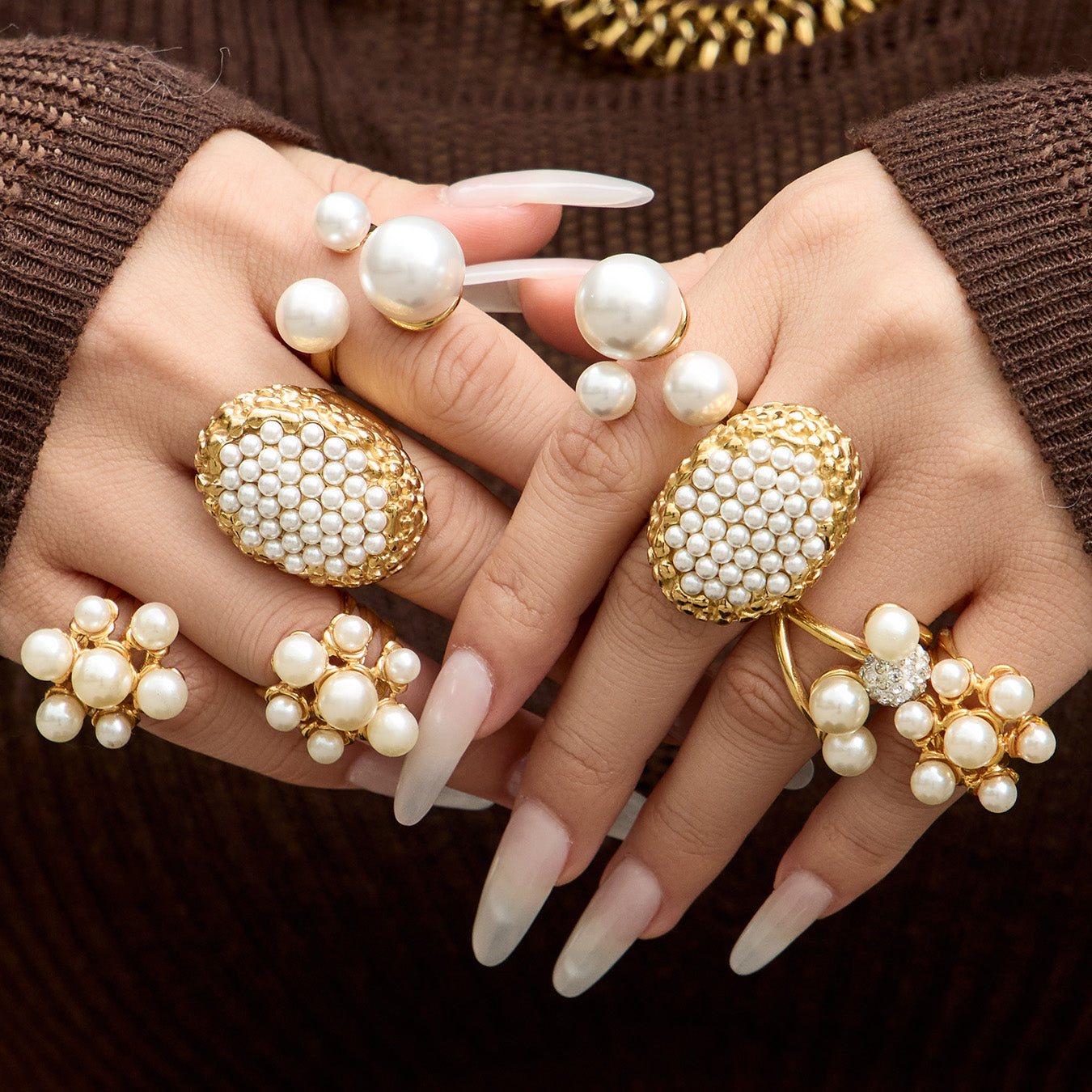 Model wearing multiple gold faux pearl statement rings against a brown background