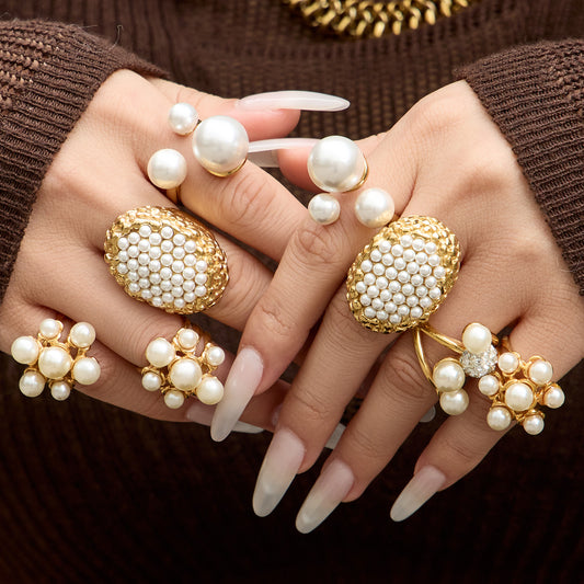 Model wearing multiple gold faux pearl statement rings against a brown background