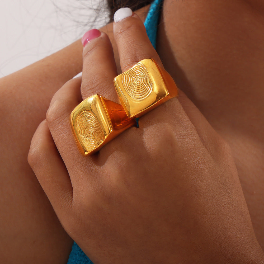 Model wearing a chunky gold-tone fingerprint statement ring with bold square design