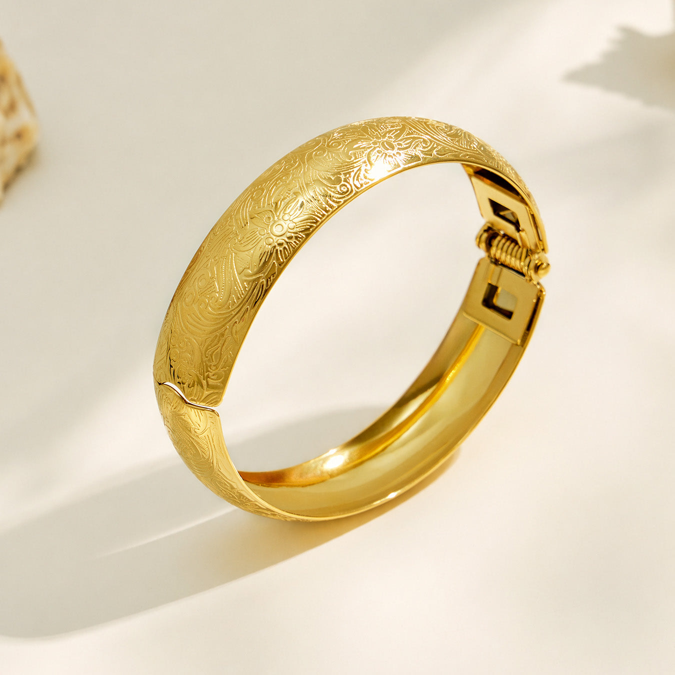Pair of gold floral engraved wide bangles in a product display