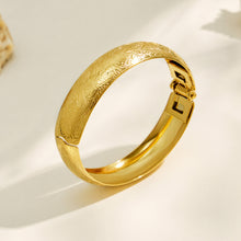 Pair of gold floral engraved wide bangles in a product display