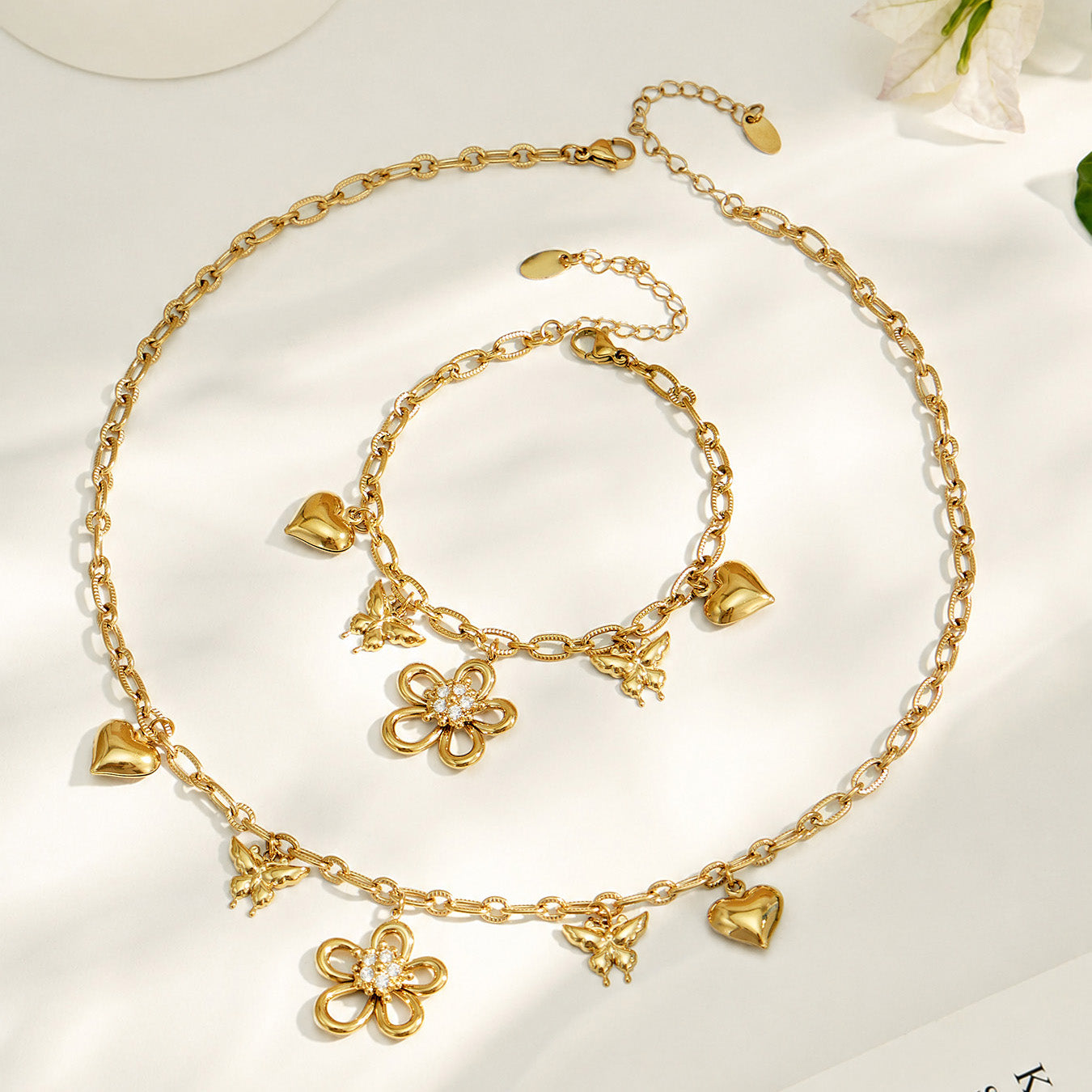 Gold floral charm necklace and matching butterfly bracelet displayed together on a light background