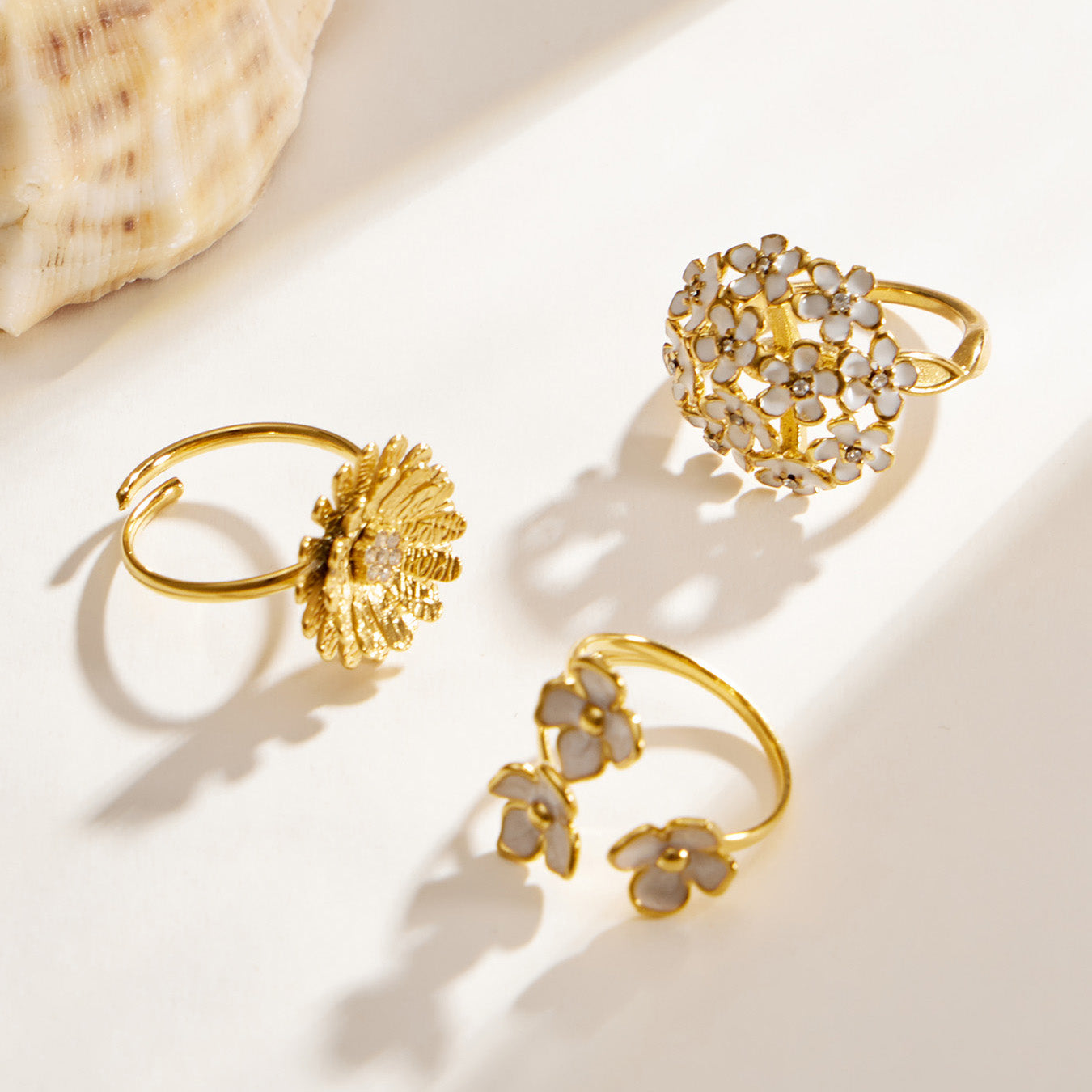 Three gold floral ring styles with daisy, enamel and cubic zirconia details displayed on a light background