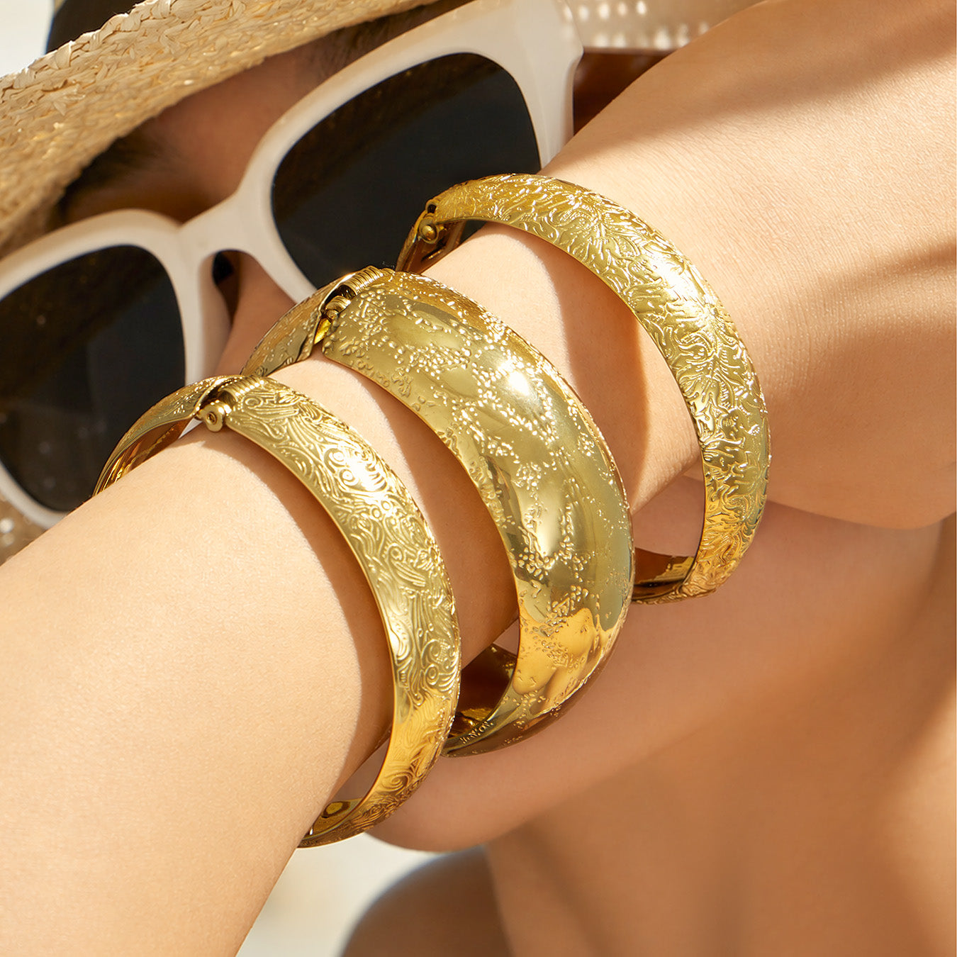 Model wearing stacked gold floral engraved wide bangles