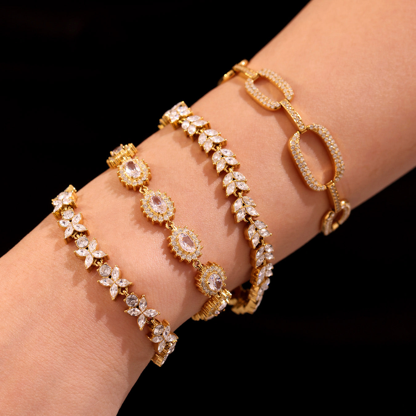 Close-up of gold floral zircon, tennis and oval link bracelets worn together