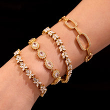 Close-up of gold floral zircon, tennis and oval link bracelets worn together
