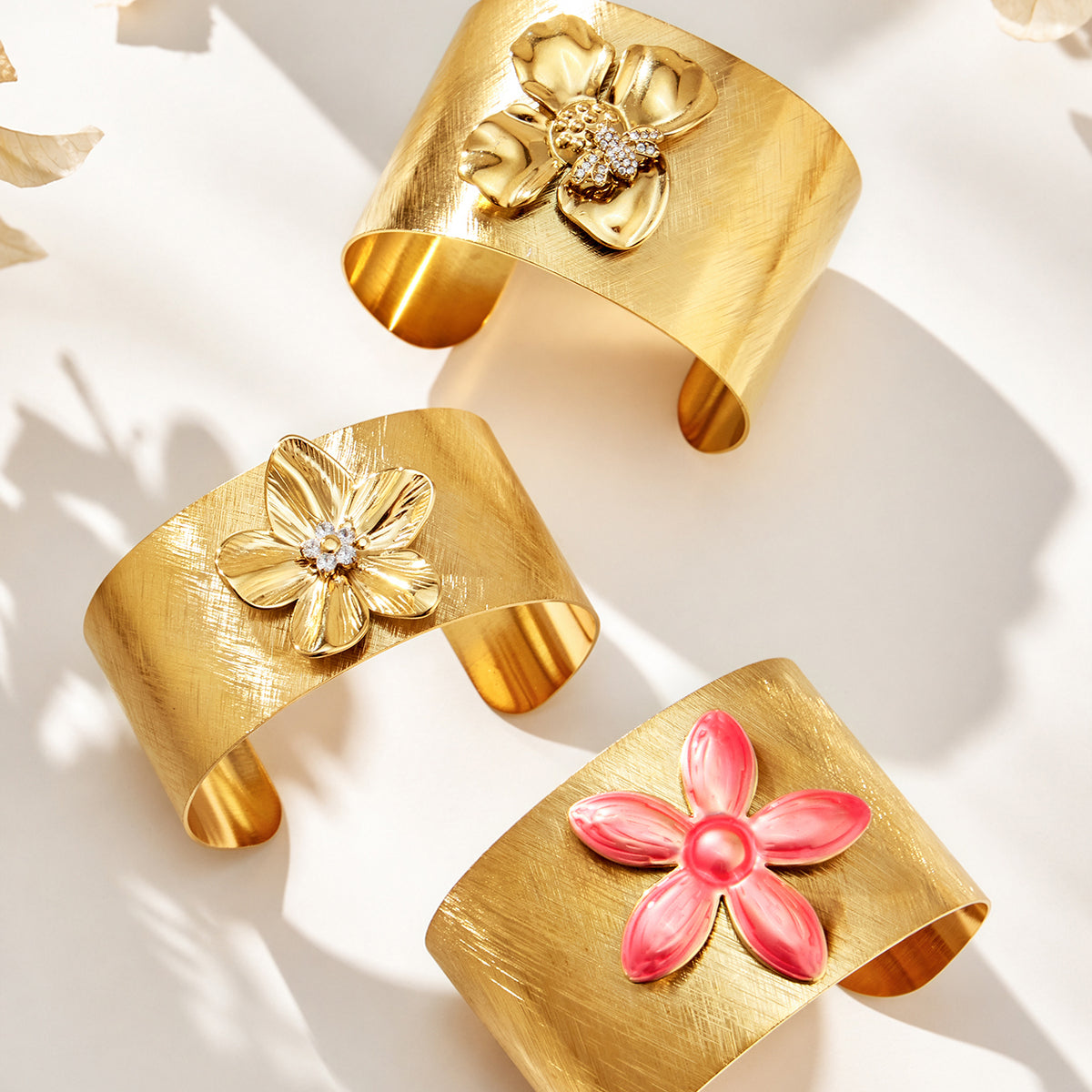 Assorted gold-tone flower cuff bangles with floral and pink decorative details