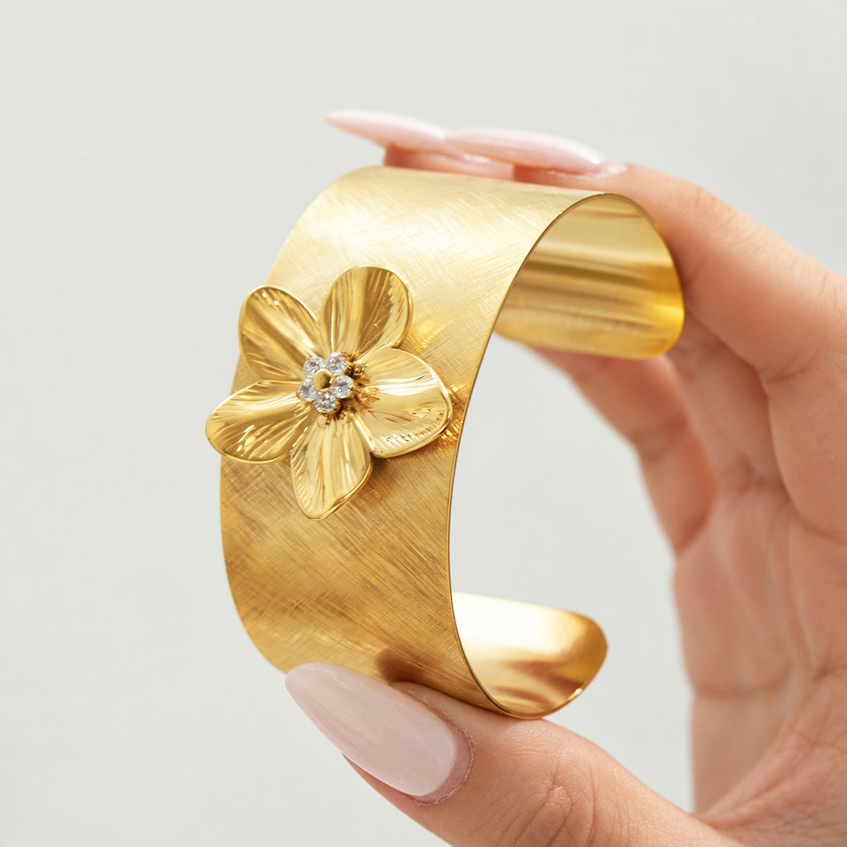 Gold flower cuff bangle with textured floral design shown close up in hand