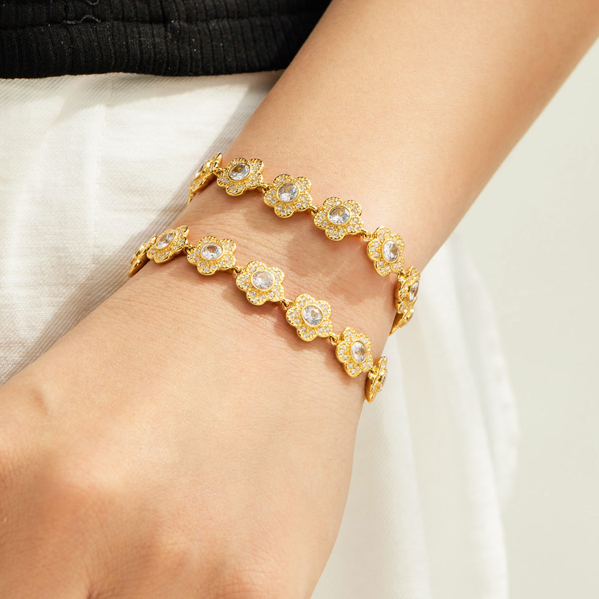Gold flower link bracelets with cubic zirconia accents layered on the wrist