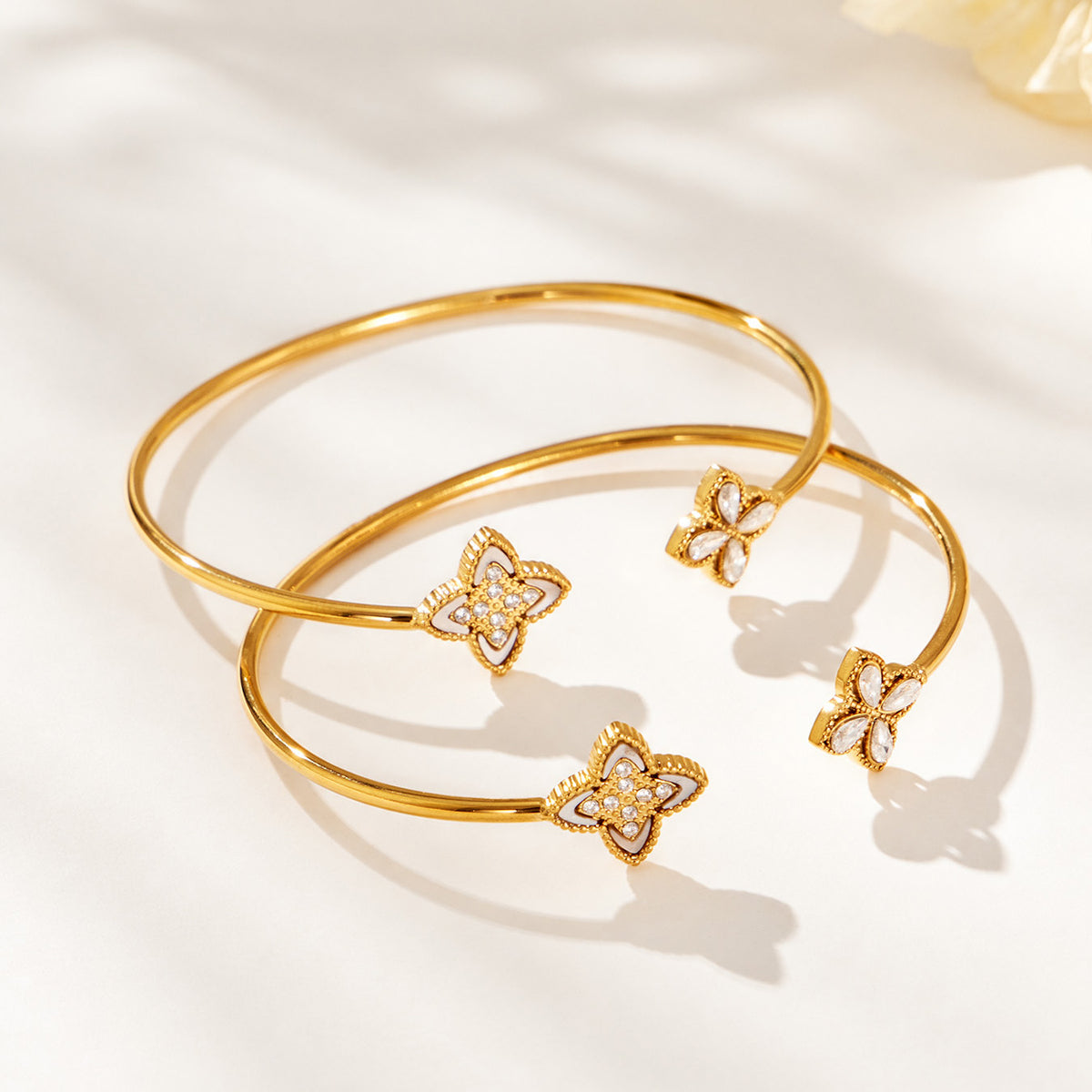 Two gold-tone open bangles with four-petal flower and zircon decorative ends