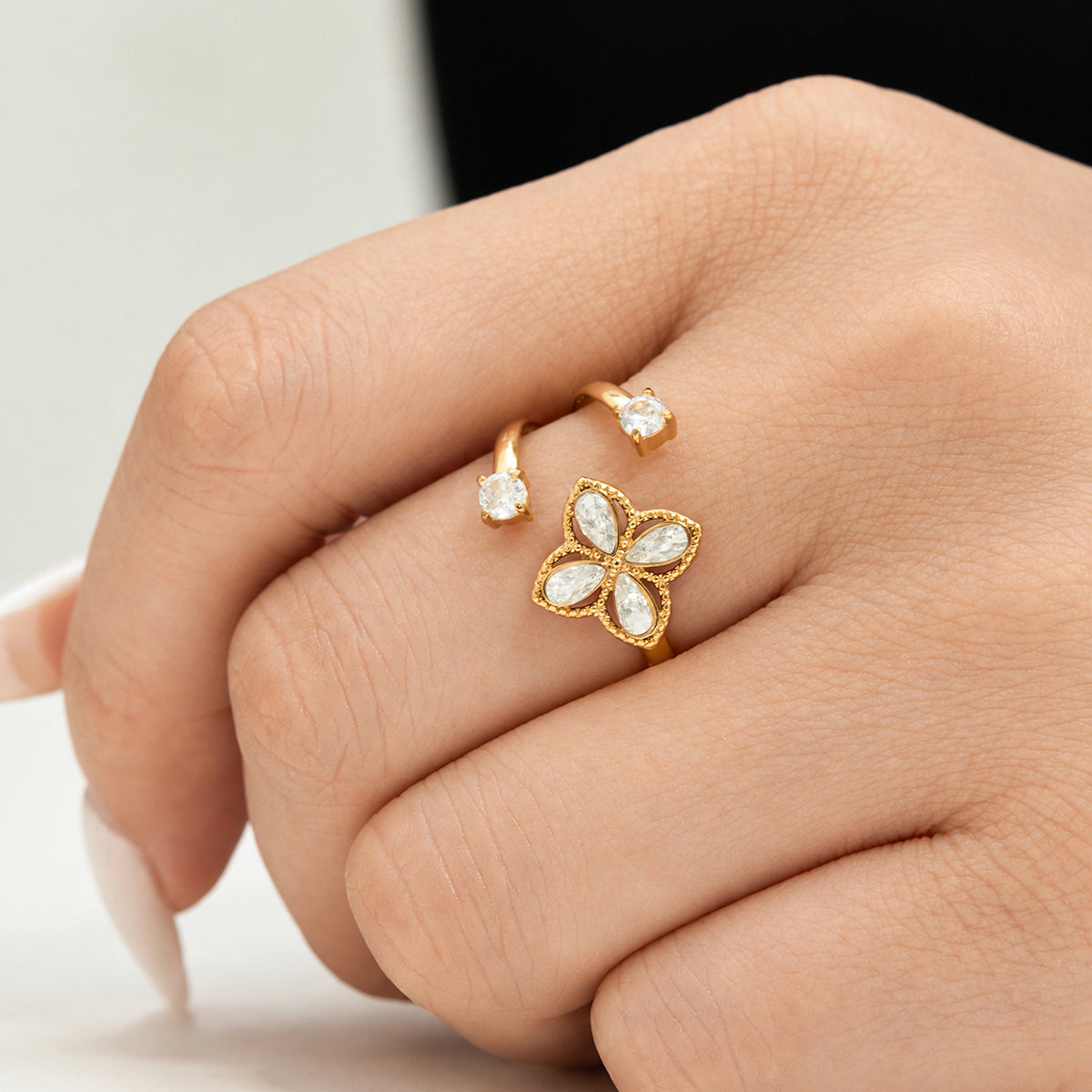 Gold-tone four-petal zircon open ring with clear stone accents shown close up on the hand