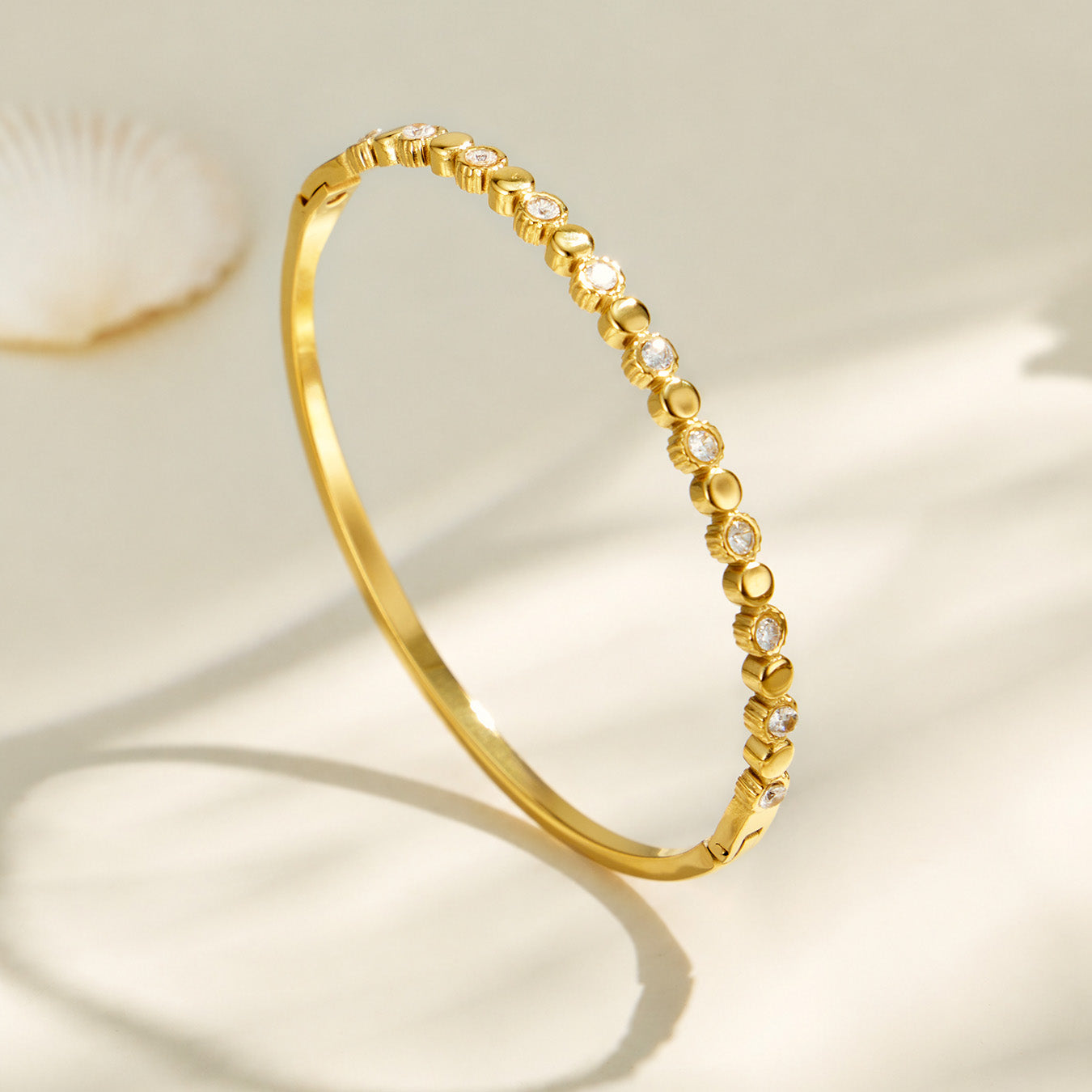 Angled product view of a gold geometric bangle with zircon accents