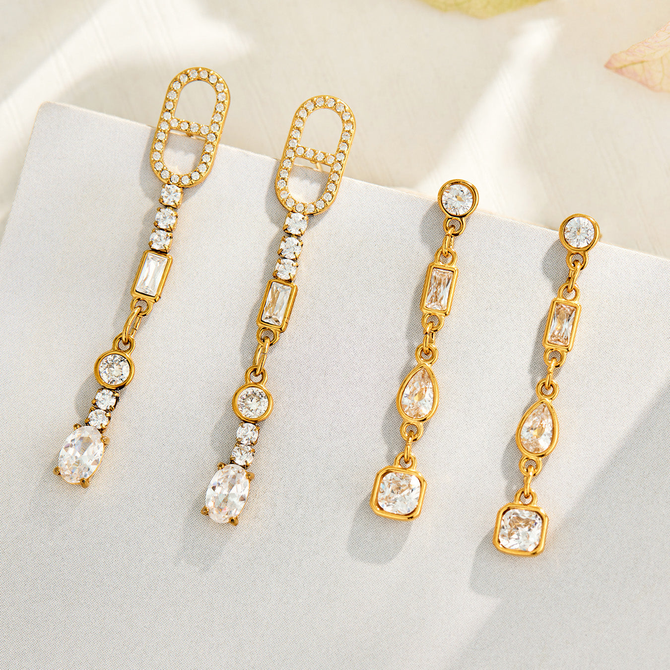 Gold geometric cubic zirconia drop earrings displayed on a neutral background