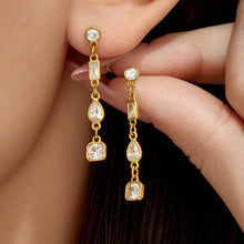 Hand holding gold geometric cubic zirconia drop earrings beside the ear