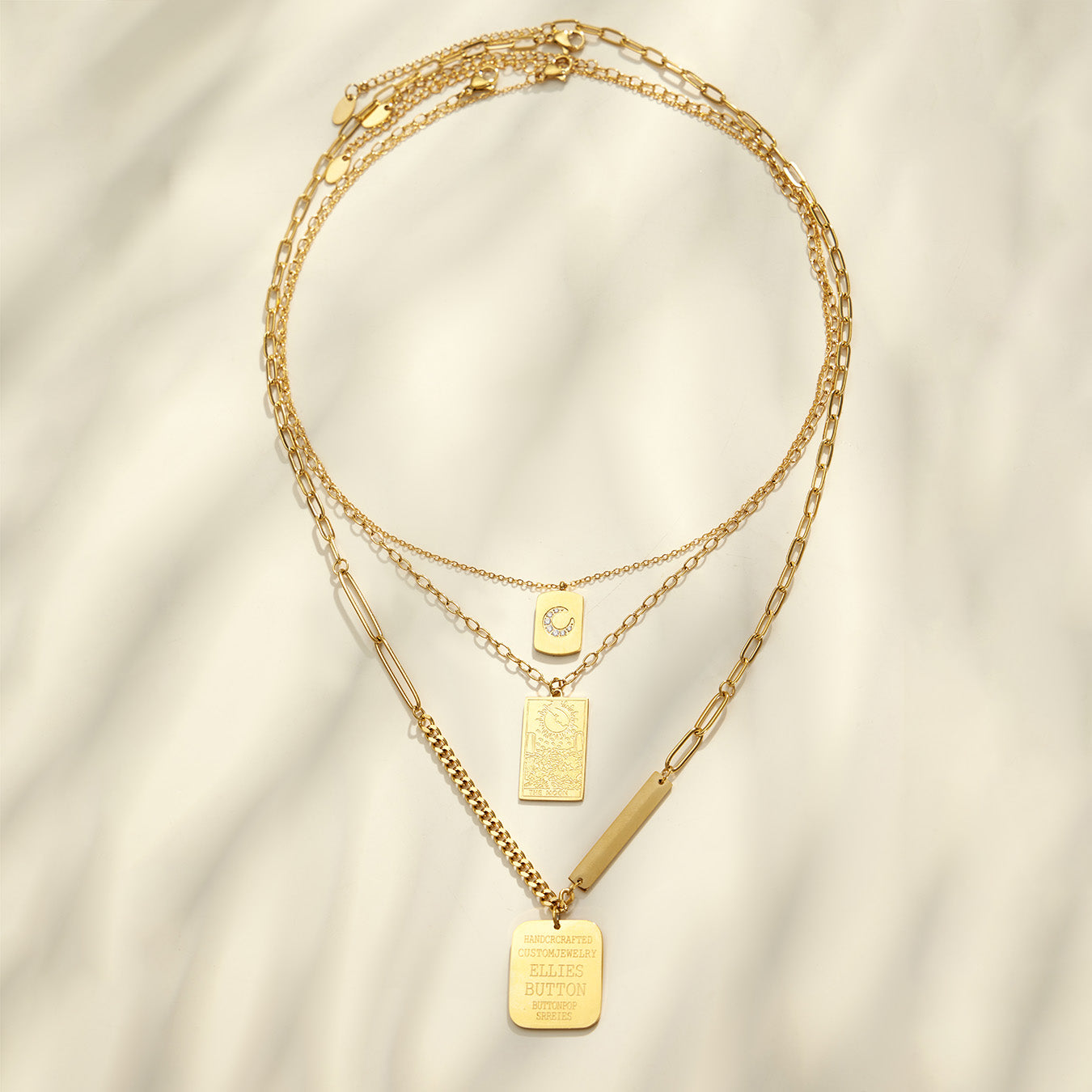 Gold square and rectangular pendant necklaces arranged in a layered flat lay