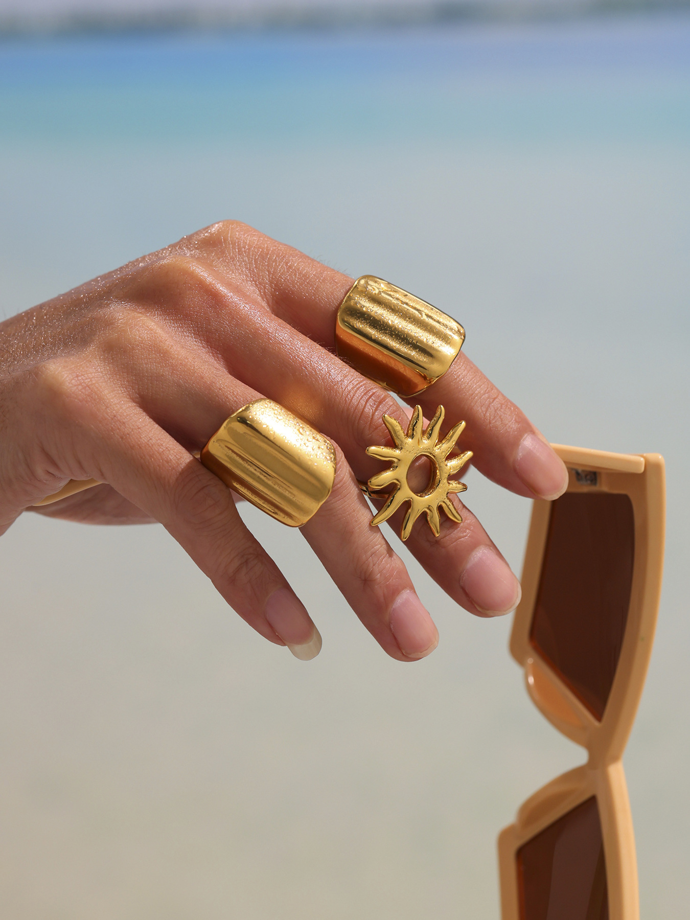 Gold geometric wide band ring close-up on hand with sunglasses for resort styling