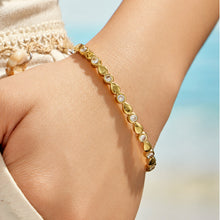 Gold geometric zircon bangle worn on a model wrist near the sea