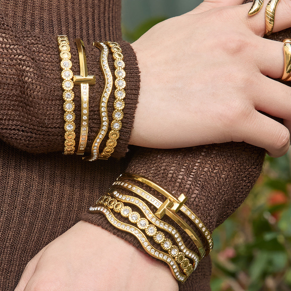 Gold zircon bangle bracelets stacked on both wrists with wavy cuff, H buckle and round zircon designs for statement jewelry styling
