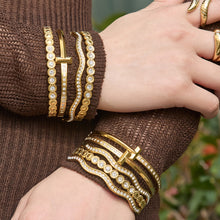 Gold zircon bangle bracelets stacked on both wrists with wavy cuff, H buckle and round zircon designs for statement jewelry styling