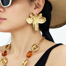 Gold hammered flower earrings with oversized floral silhouette worn on ear