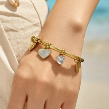 Close-up wrist view of a gold heart bangle bracelet with dangling charms