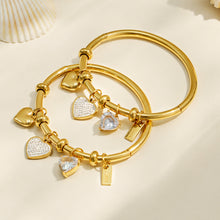 Gold heart charm bangle bracelet displayed in a neutral flat lay