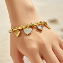 Gold heart charm bangle bracelet shown on a model hand in natural light