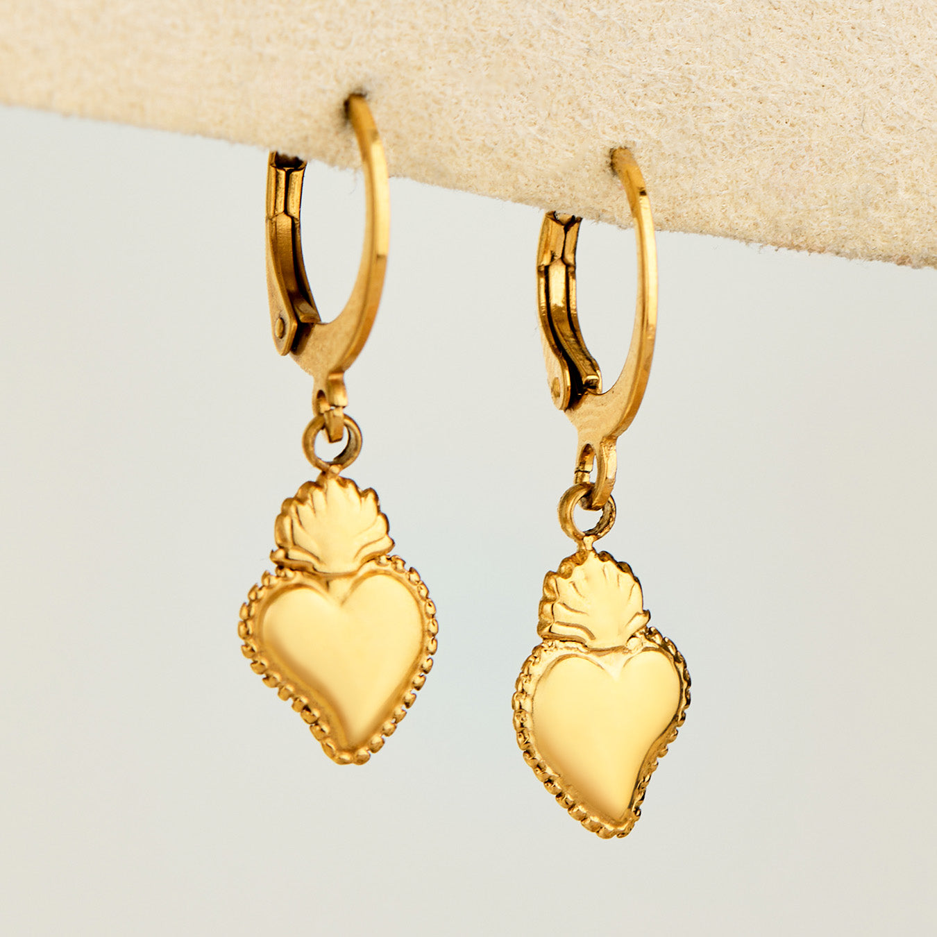 Pair of gold heart charm huggie earrings displayed on a neutral jewelry stand