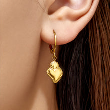Close-up of a model wearing a gold heart charm huggie earring on the earlobe