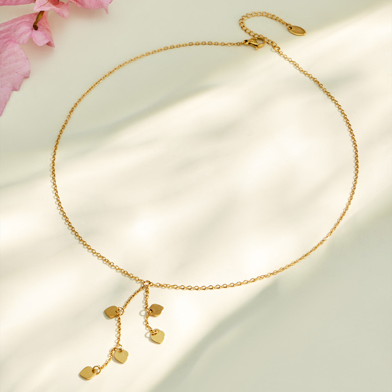 Gold heart drop Y necklace arranged in a circular flat lay with dangling charms