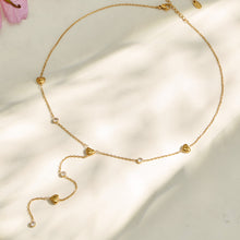 Gold heart lariat necklace arranged on soft neutral fabric with a long curved chain drop