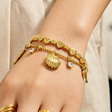 Model wearing layered hammered heart-link and ocean charm bracelets