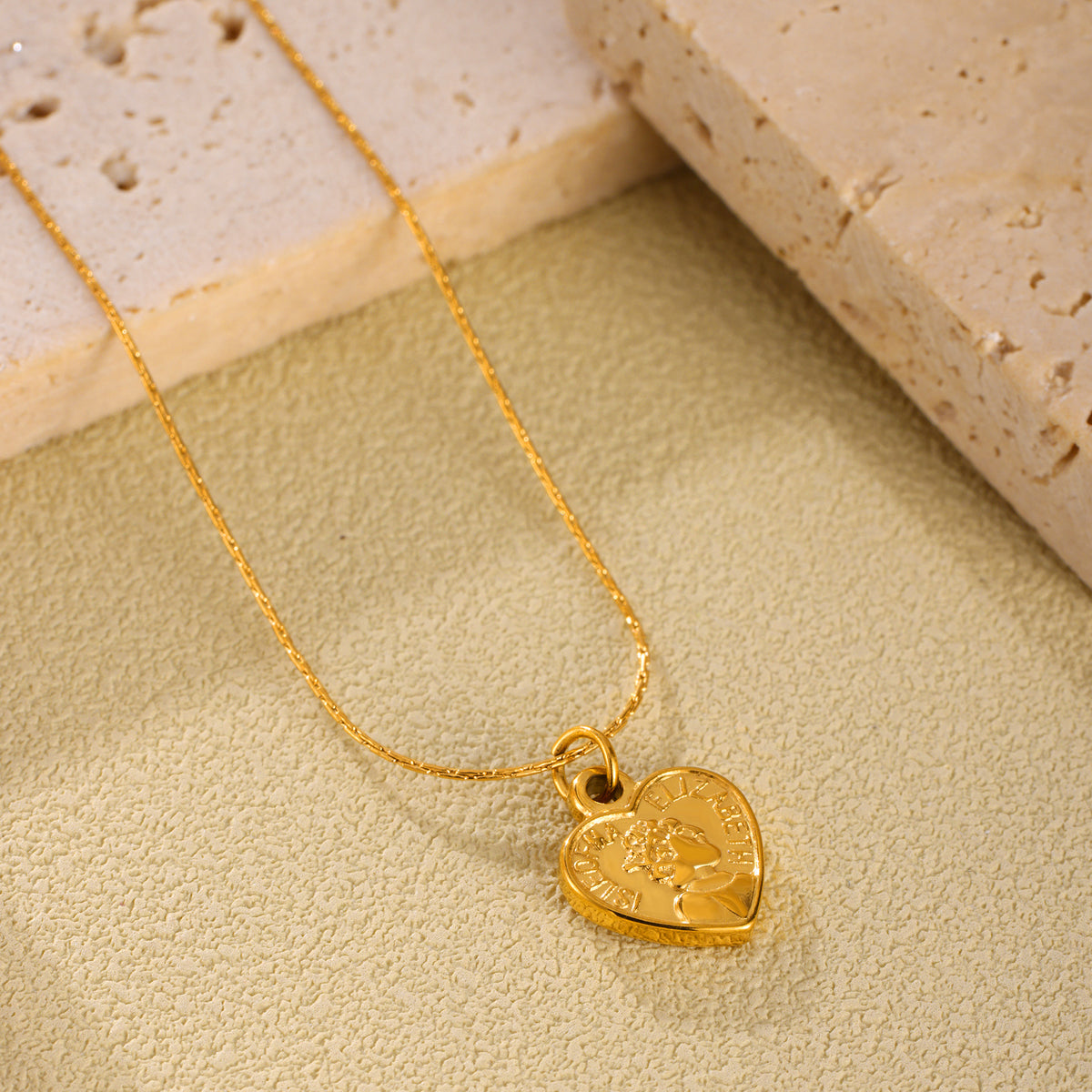 Close-up flat lay of a textured gold heart pendant necklace on a warm neutral surface
