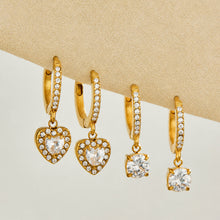 Gold heart and round CZ charm huggie earrings displayed on a neutral background