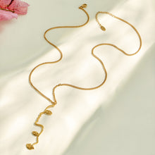 Gold heart tassel Y necklace arranged in a flowing flat lay on neutral fabric