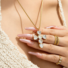 Gold heart-stone zircon cross necklace held by model in close-up