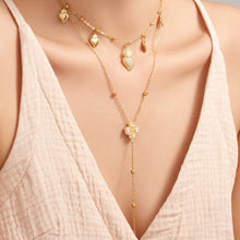 Gold heart zircon charm necklace layered with a four-petal flower zircon Y necklace on model