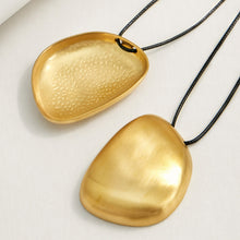 Close-up of smooth gold irregular pebble pendants with black cord details