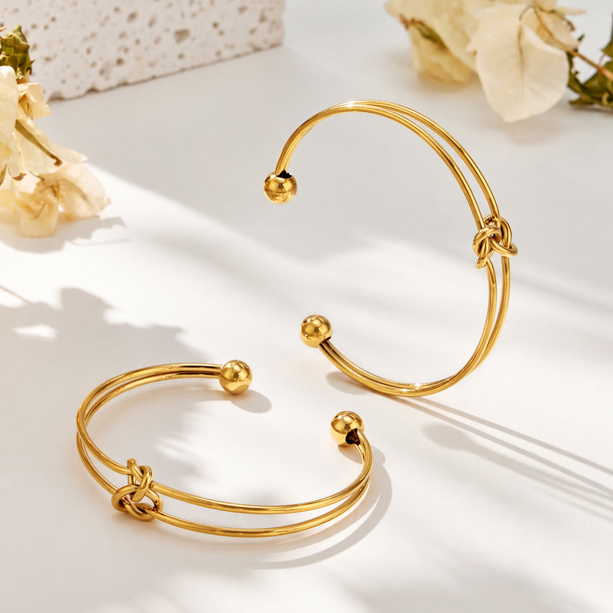 Two gold-tone knot cuff bracelets shown at different angles with open cuff structures