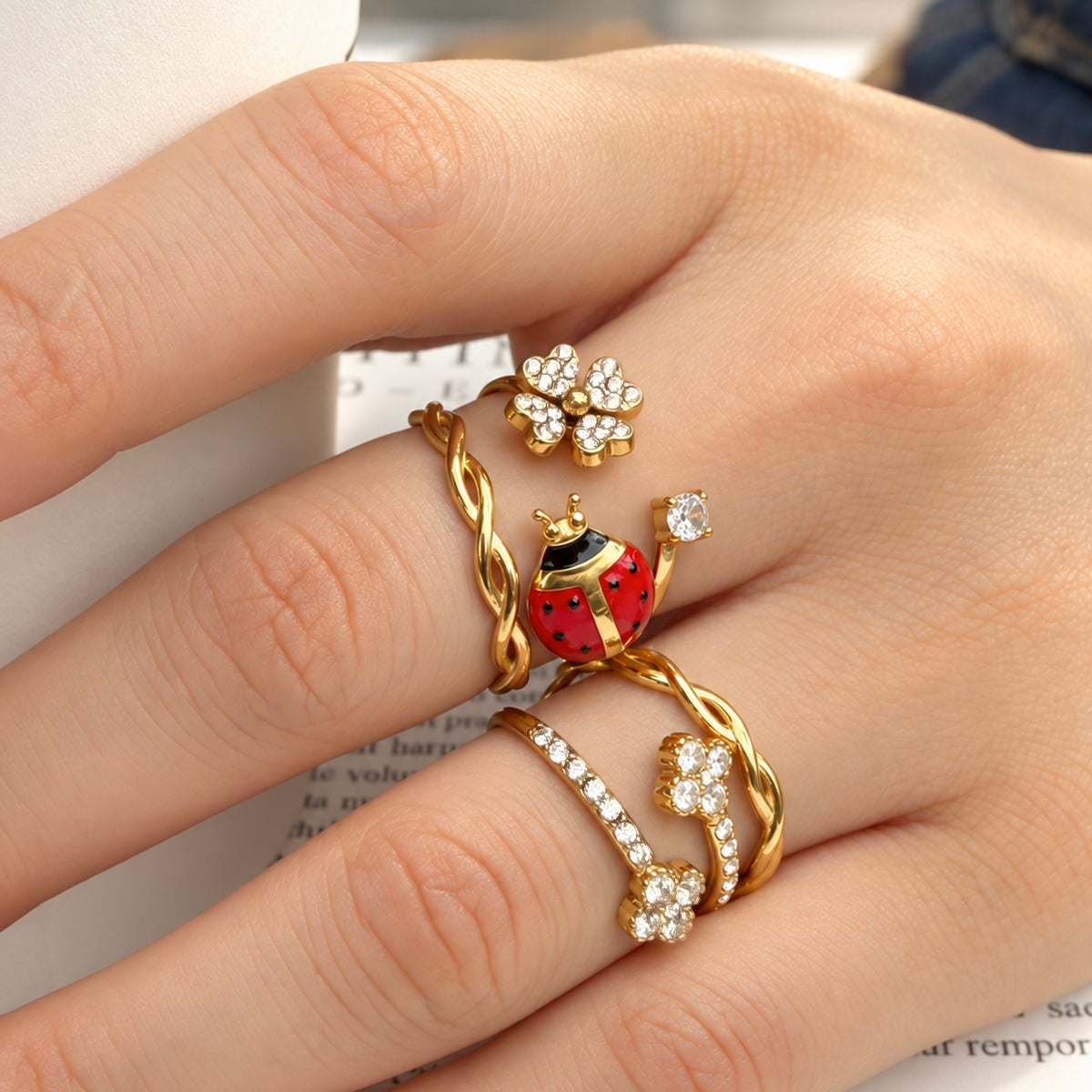 Close-up of gold-tone stainless steel ladybug, double-flower and twisted band rings worn across fingers