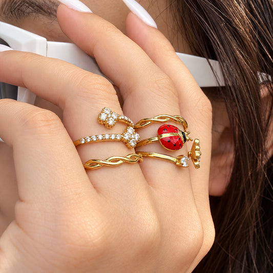 Gold-tone ladybug, double-flower and twisted band rings worn together on a hand holding a white cup