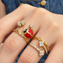 Gold-tone ladybug and double-flower rings paired with slim twisted bands in a close-up hand view