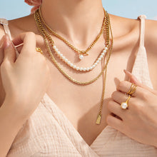 Model touching layered gold necklaces with faux pearl and minimalist chain details