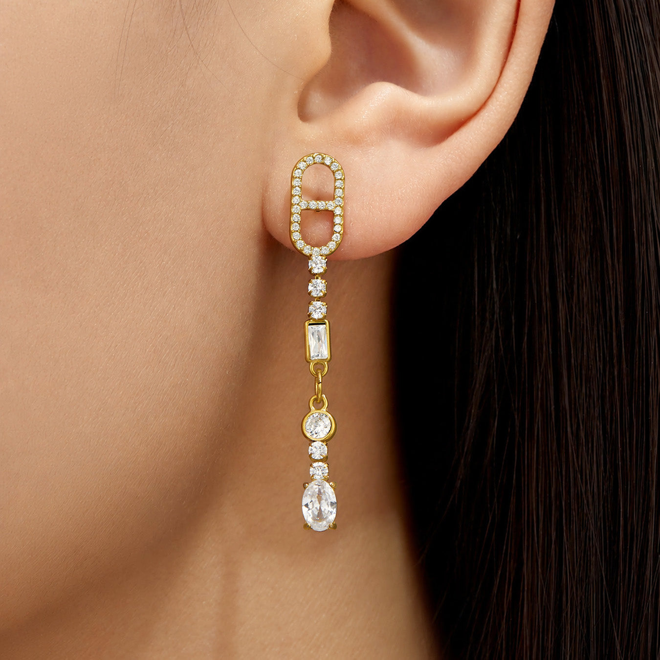 Model wearing long gold cubic zirconia drop earrings with clear stone accents